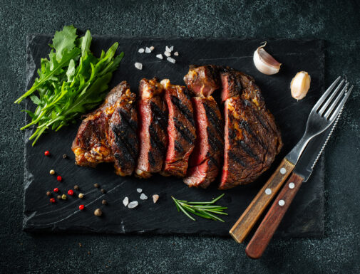 Sliced steak ribeye, grilled with pepper, garlic, salt and thyme served on a slate chopping Board on a dark stone background. Top view. Flat lay.